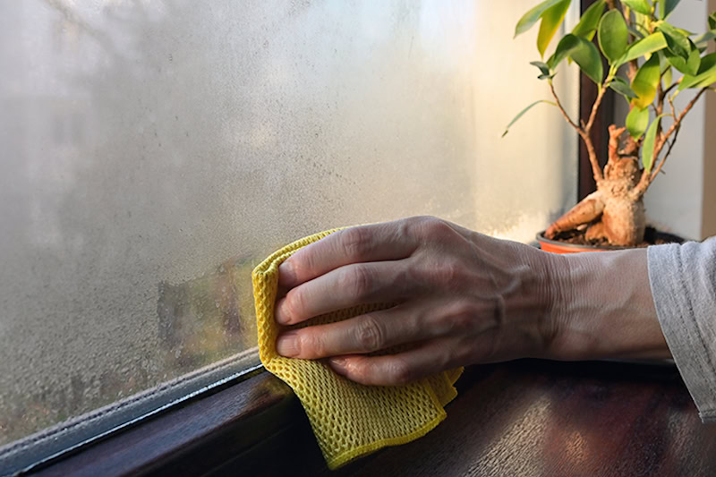 hand wiping condensation off of a window in a kitchen.